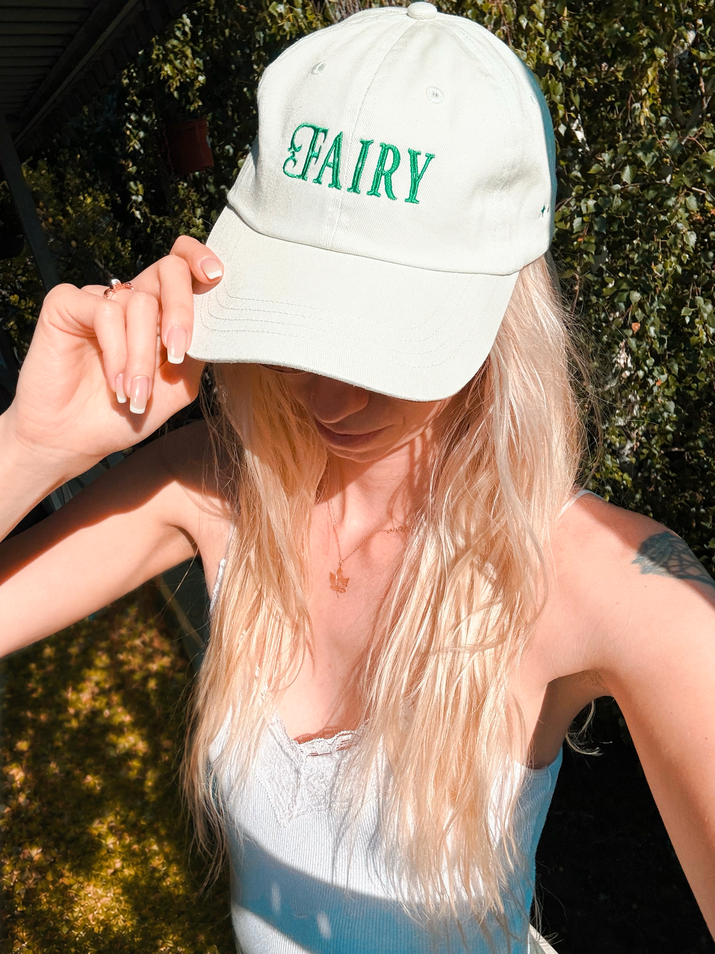 Person wearing a pastel green cap with 'FAIRY' in green whimsical text outdoors.