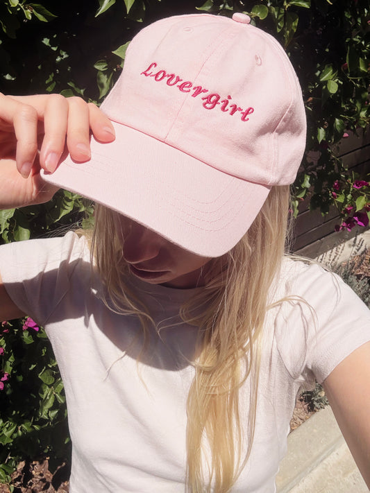Person wearing a pink cap with 'Lovergirl' text outdoors.